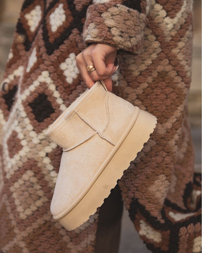 Beige slip-on shoe held by a person wearing a patterned coat.